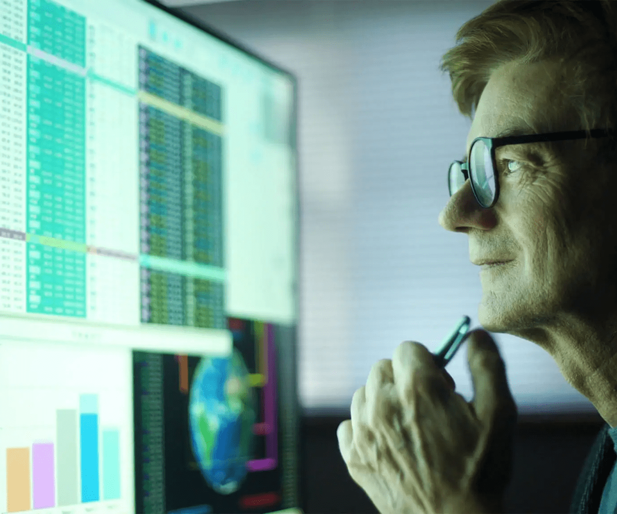 Man analyzing data on computer screens in a dimly lit room.