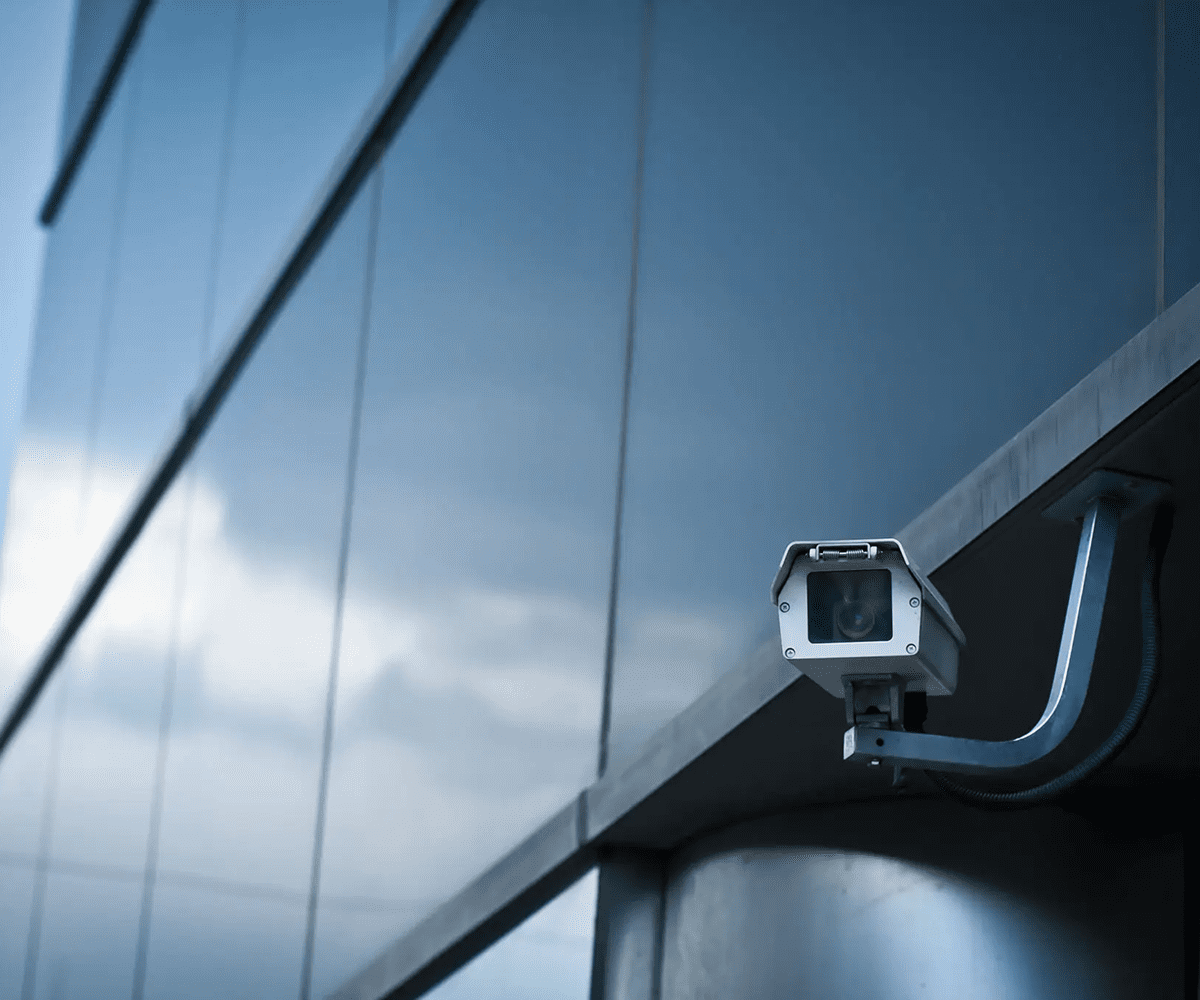 A white security camera mounted on a modern building exterior.