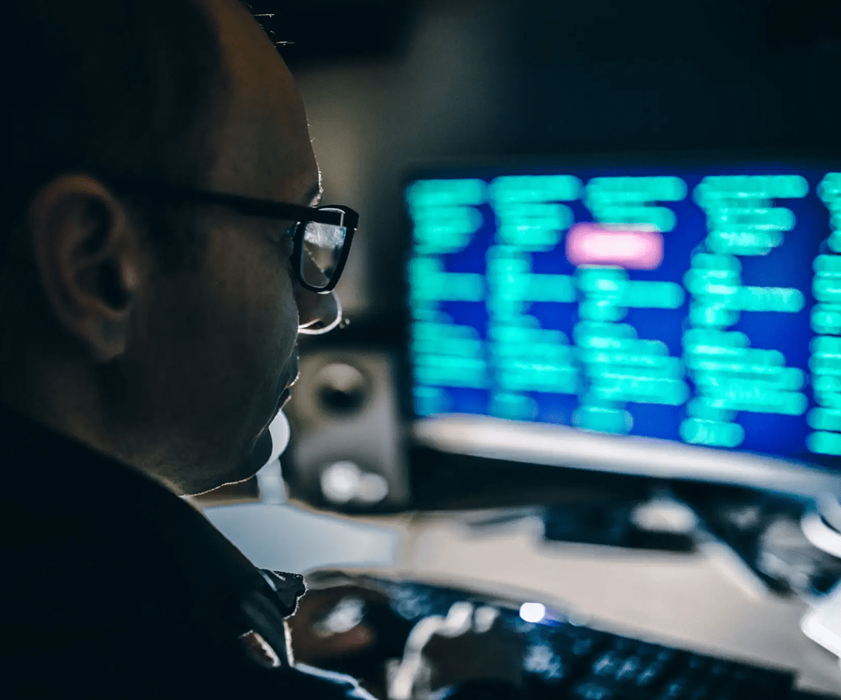 Man working on computer with code on the screen in a dark room.